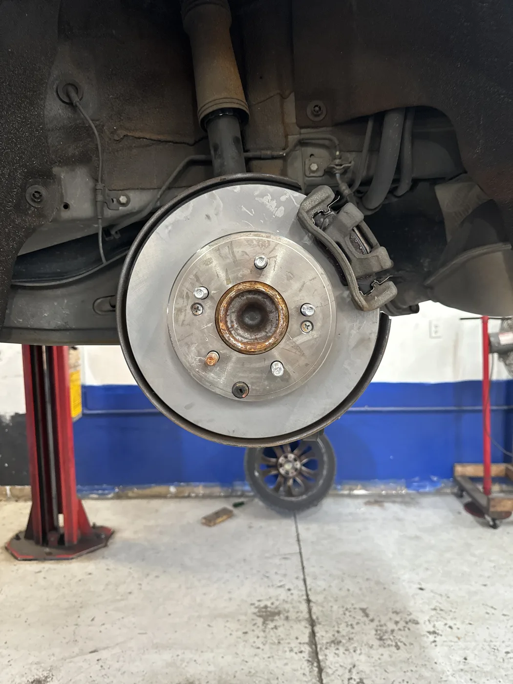 Close-up of a brake rotor and hub with the wheel removed at RepairTech Automotive in Kissimmee, showing a wear lip at the outer edge, surface scoring and the caliper bracket with pads in place