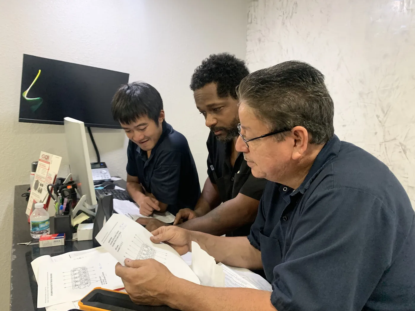 Three RepairTech Automotive technicians studying printed wiring diagrams together at the Kissimmee shop while diagnosing a fault